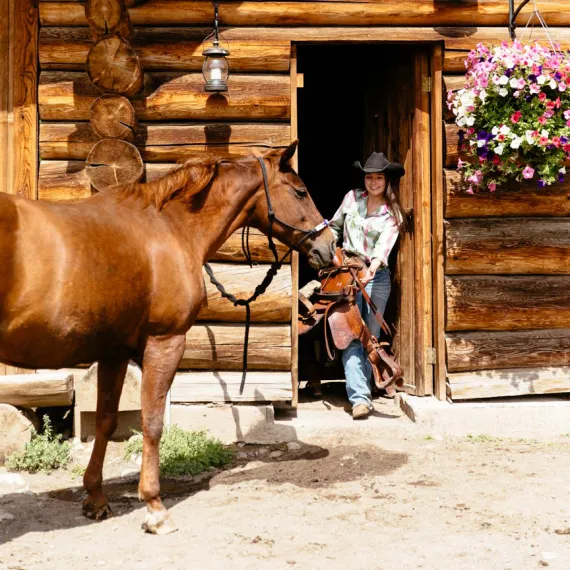 A cowgirl and her horse at the barn while enjoying a luxury dude ranch vacation at Siwash Lake.