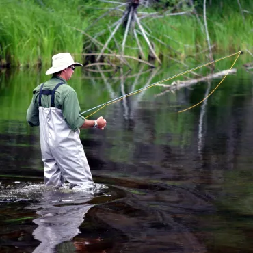 A man casts for trout while fly fishing on a wilderness river